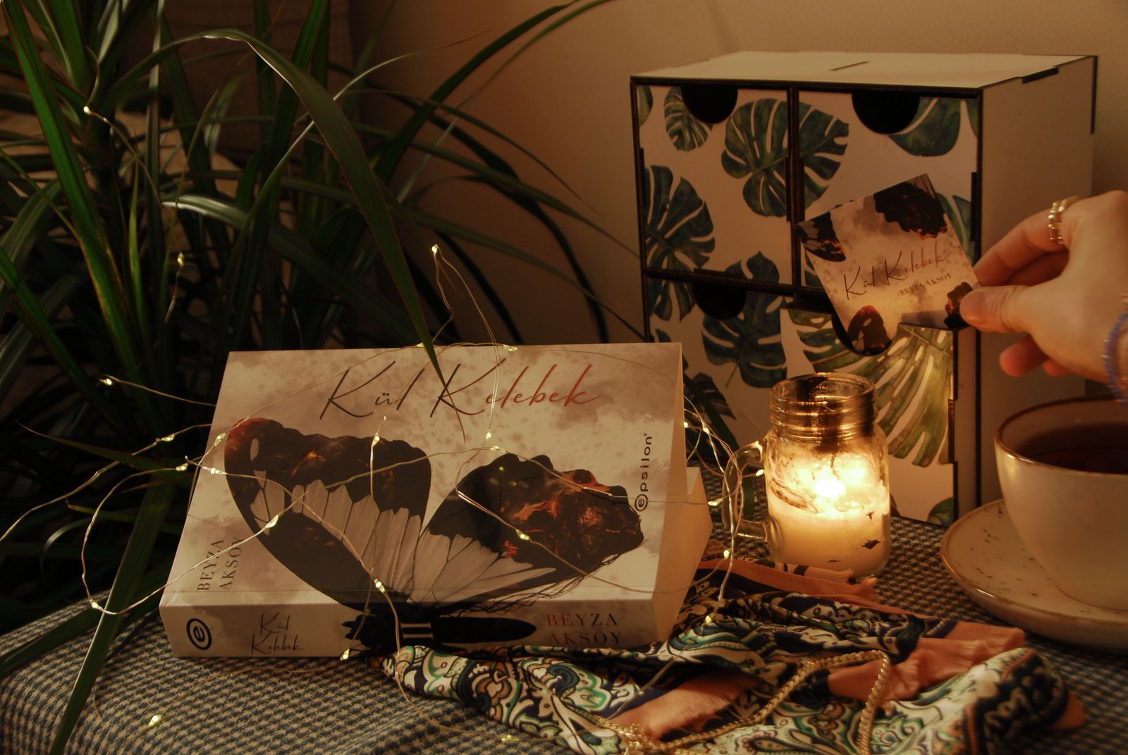 An unlit candle placed beside a stack of books on a wooden table