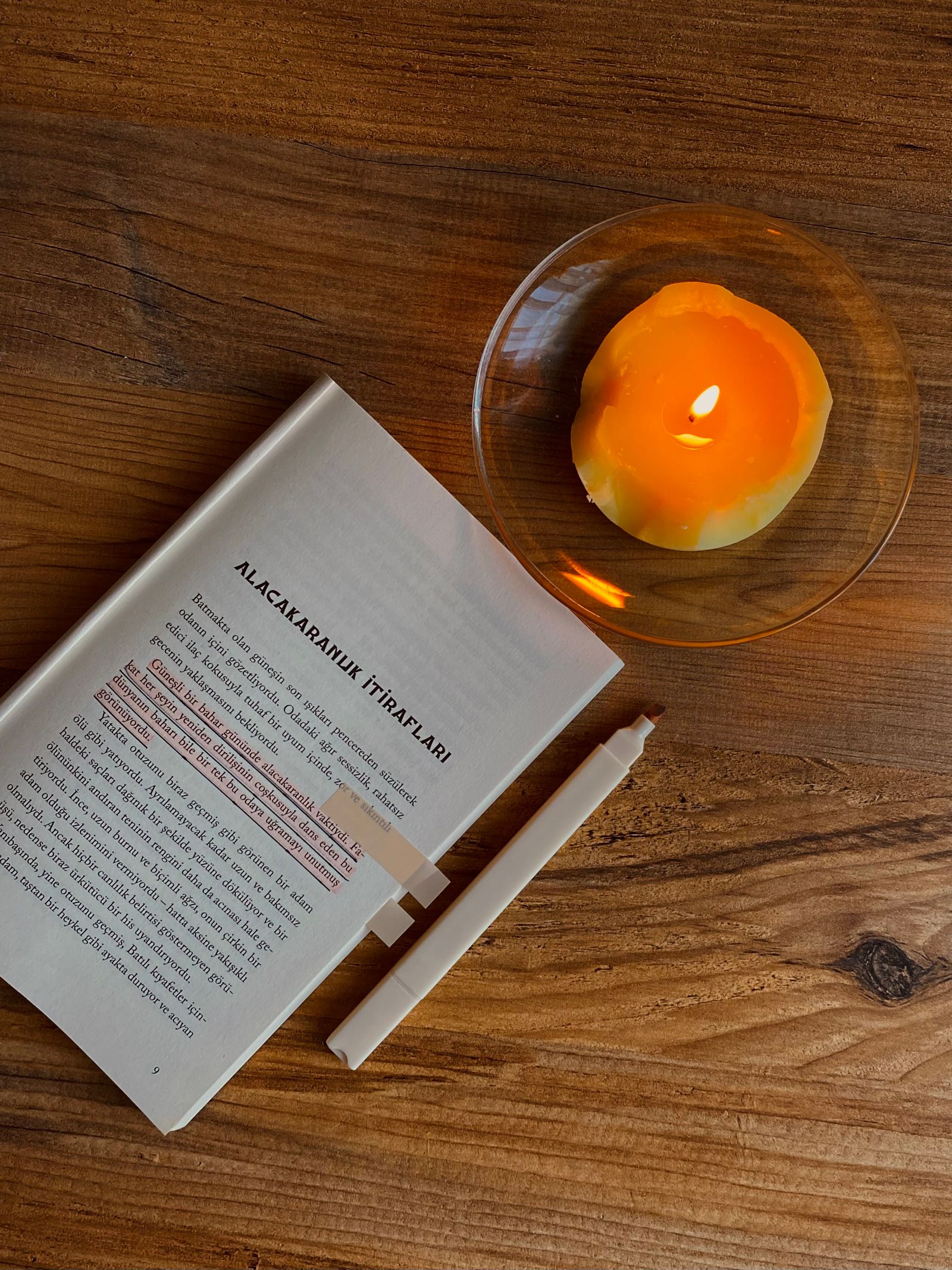 A cozy reading setup with a lit candle, an open book and a warm blanket
