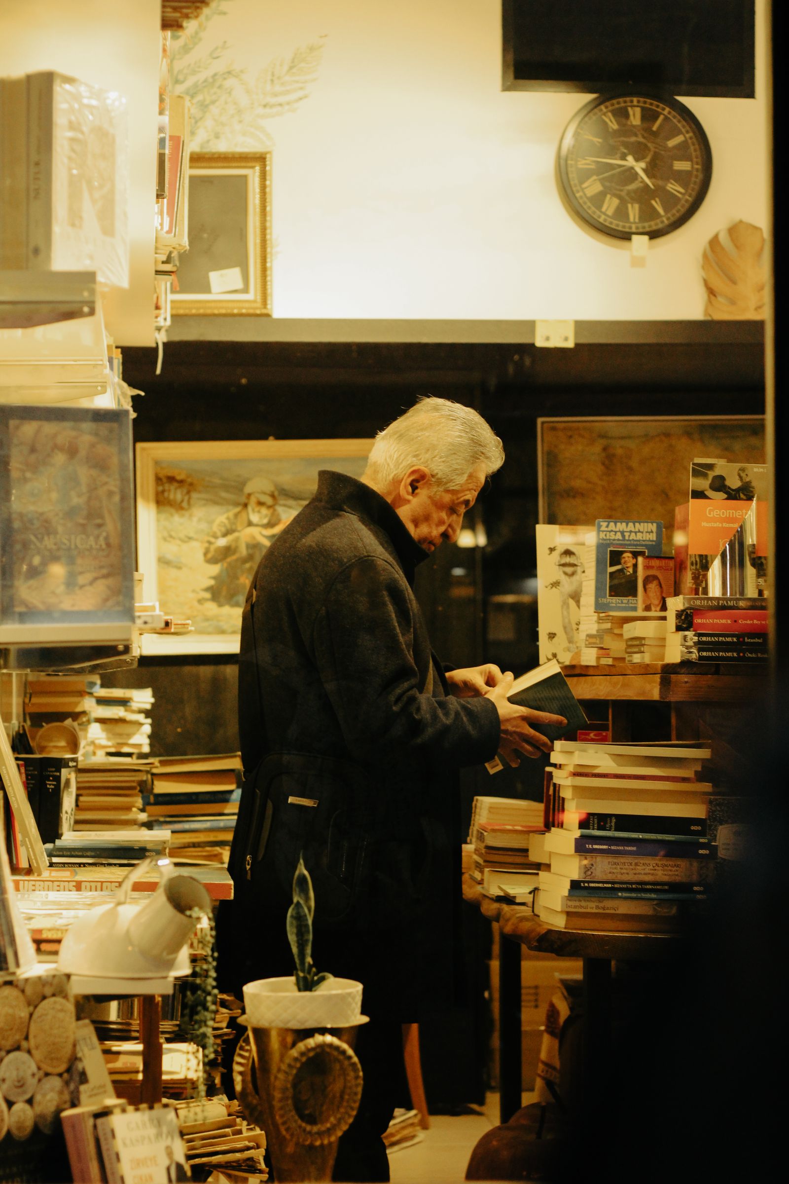 A senior man examining books in a warmly lit antiquarian bookshop filled with vintage items