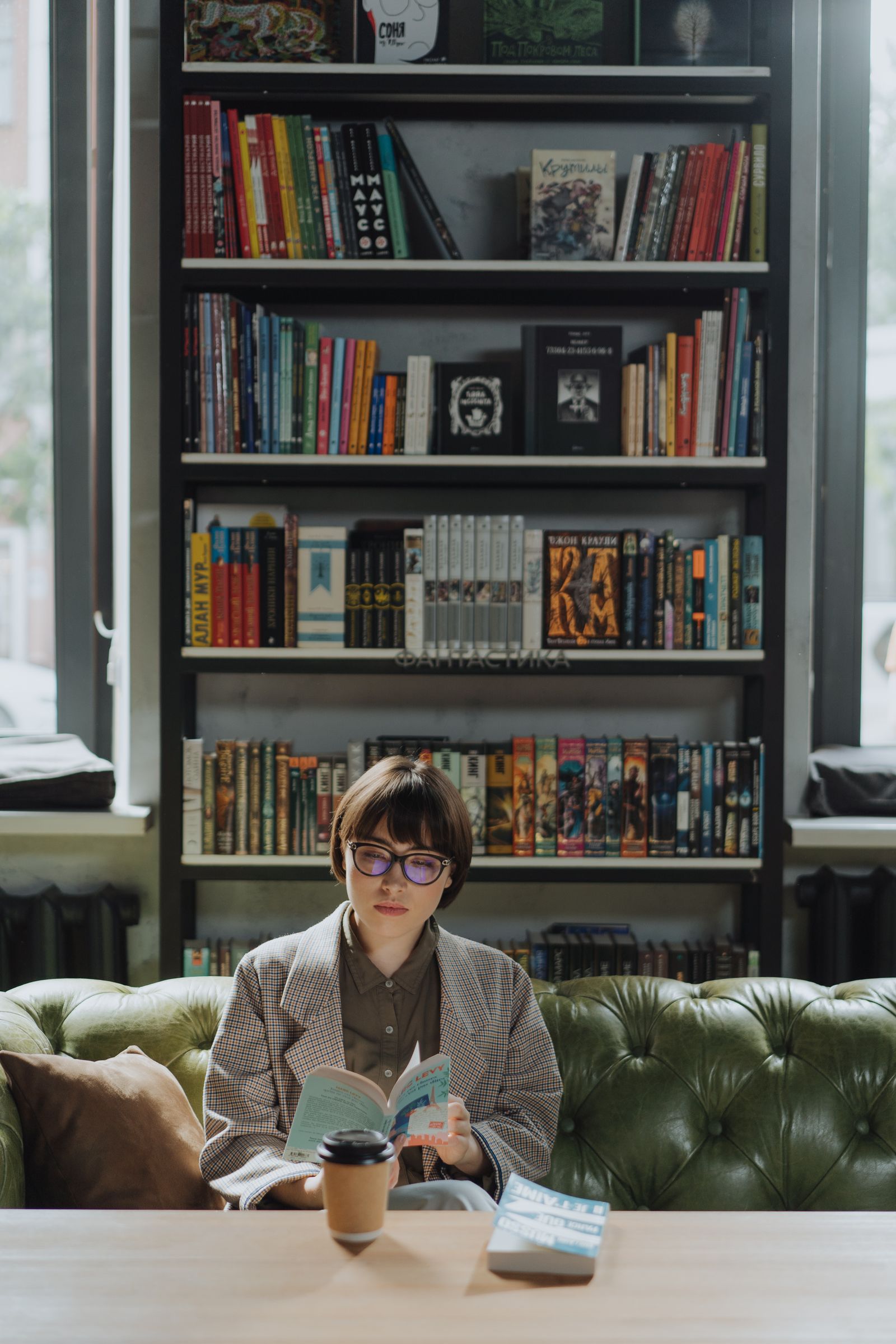 A young woman reading on a sofa in a cozy library surrounded by books