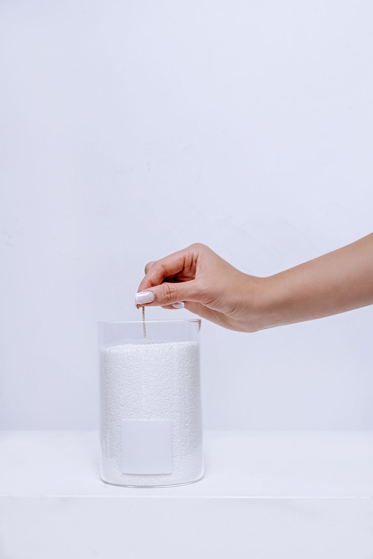A candle wick being centered into a glass jar filled with unmelted white candle wax pellets before pouring