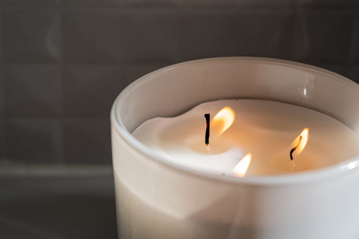 A three-wick candle burning with wax melted evenly out to the container's edge, forming a full melt pool