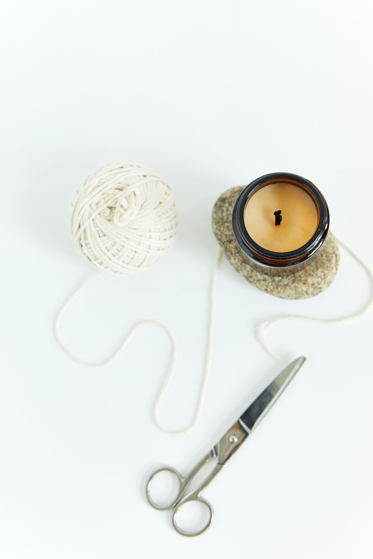A ball of cotton candle wick, an unlit candle and a pair of scissors used for wick trimming, laid out together