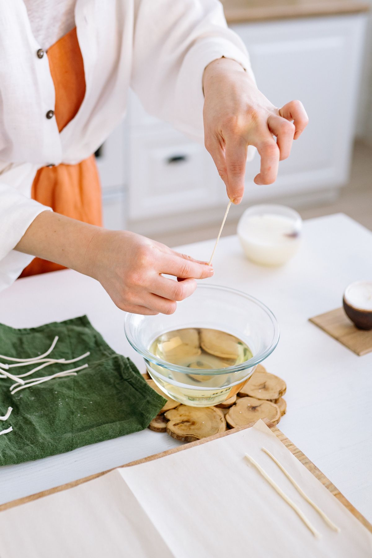 Melted candle wax being poured into a glass jar around a centered wick during hand-pouring