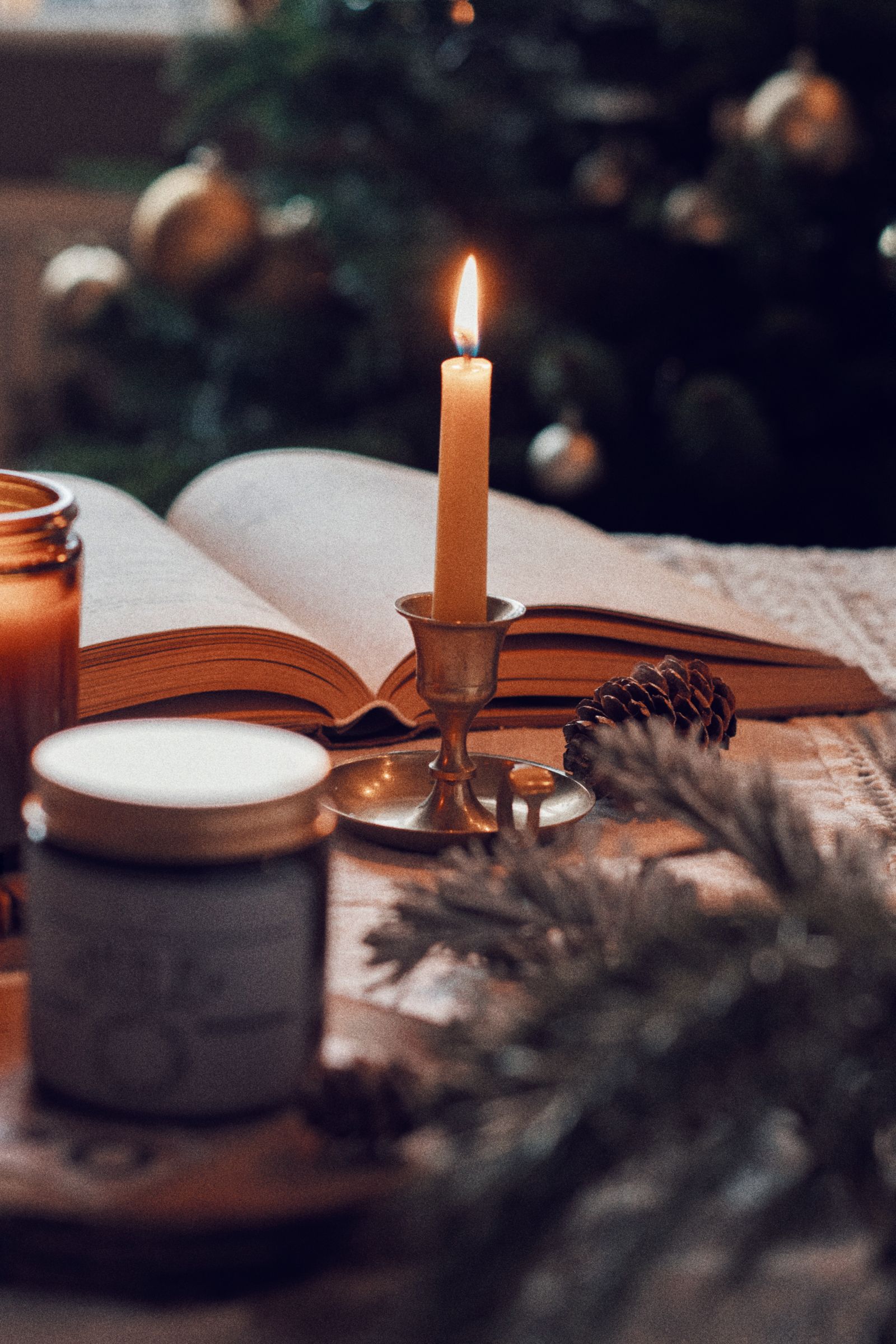 A lit candle beside an open book with festive holiday decor