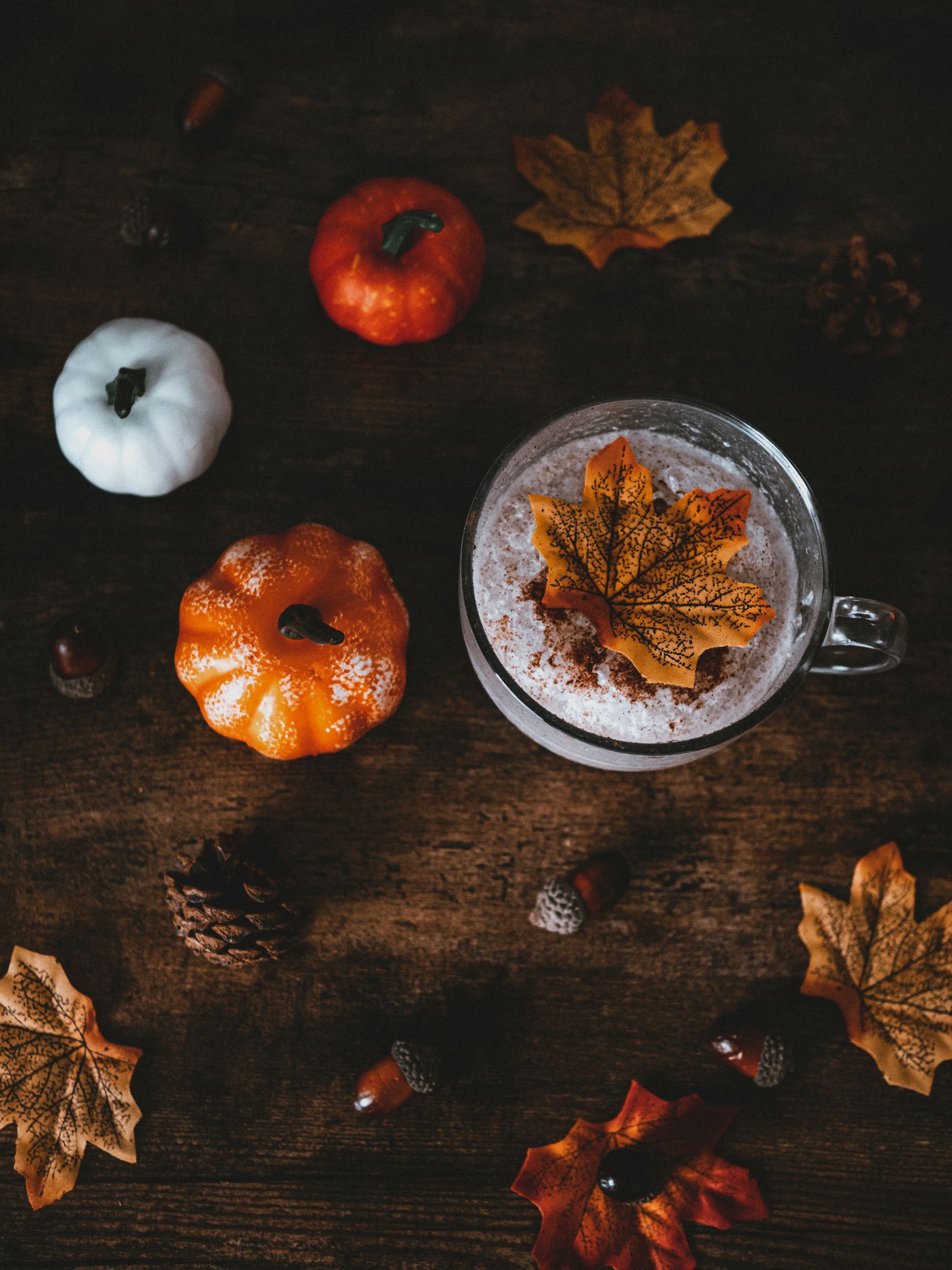A cup of coffee next to small pumpkins and autumn leaves on a wooden table