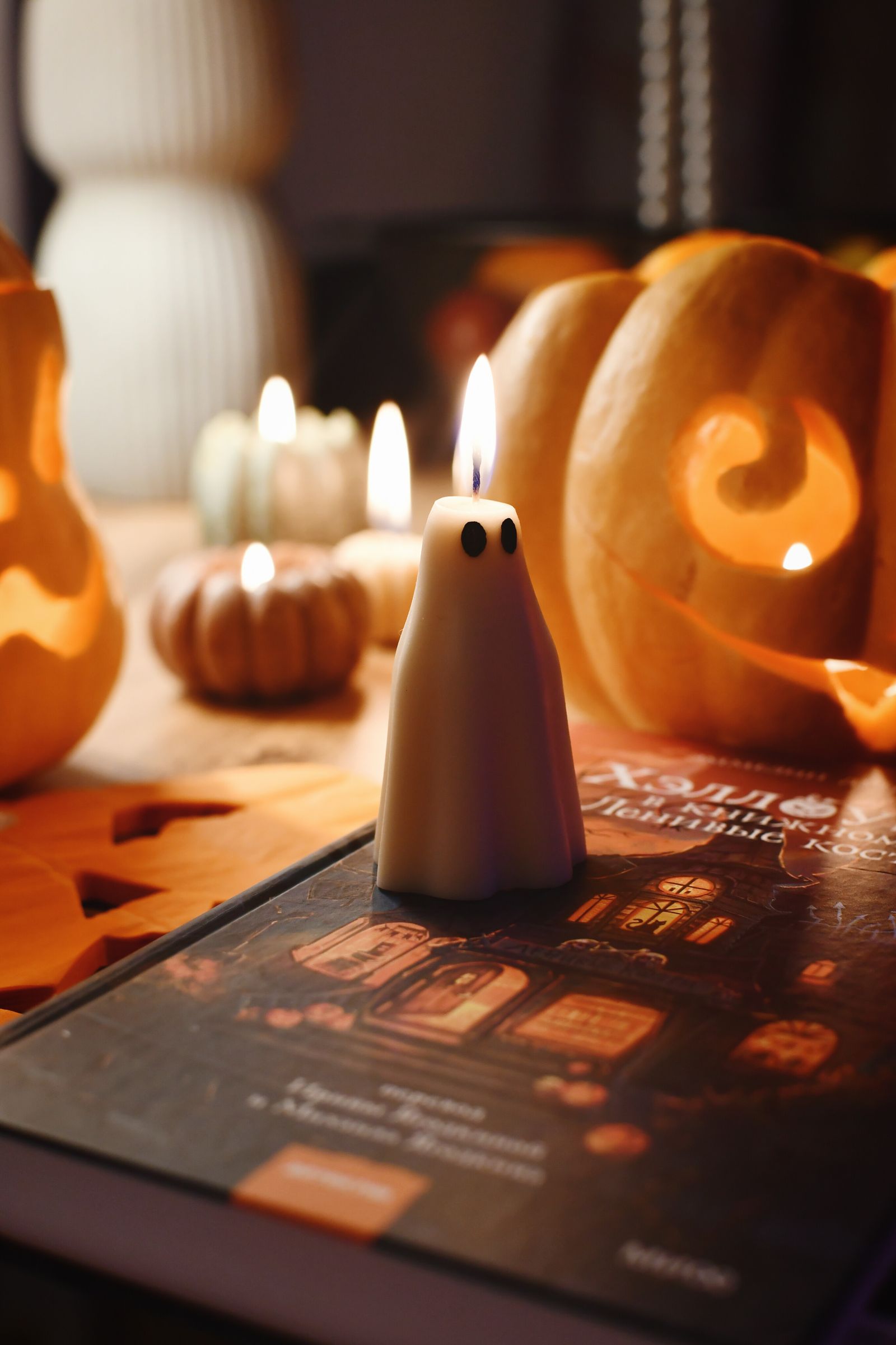 A spooky Halloween candle glowing beside carved pumpkins in a dark room