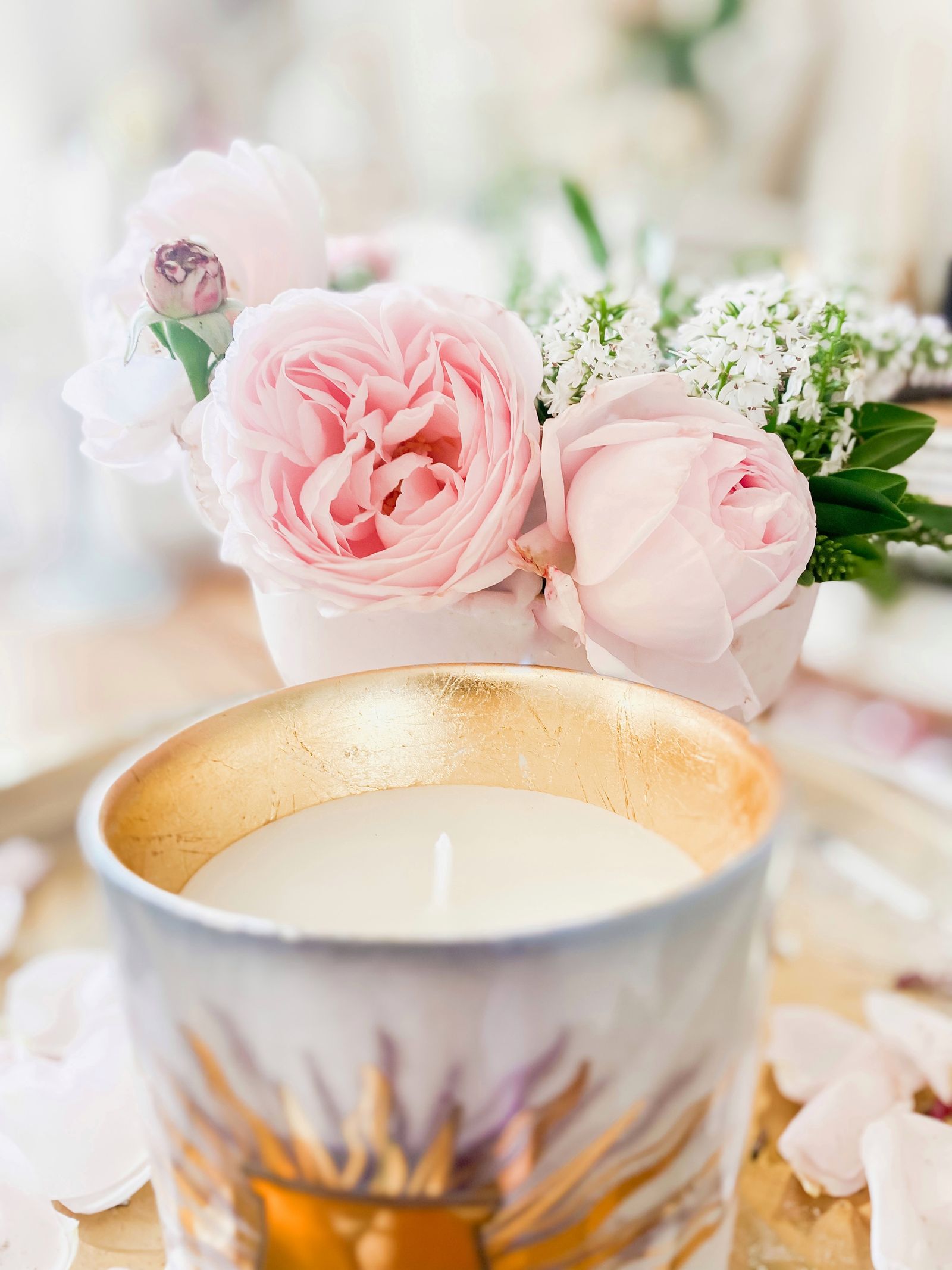 A close-up of pink roses in a vase beside a decorative candle