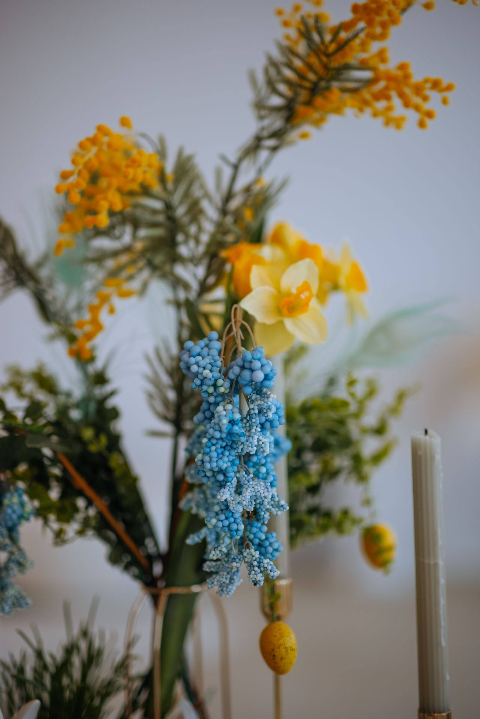 A spring floral arrangement with blue and yellow flowers beside decorative candles